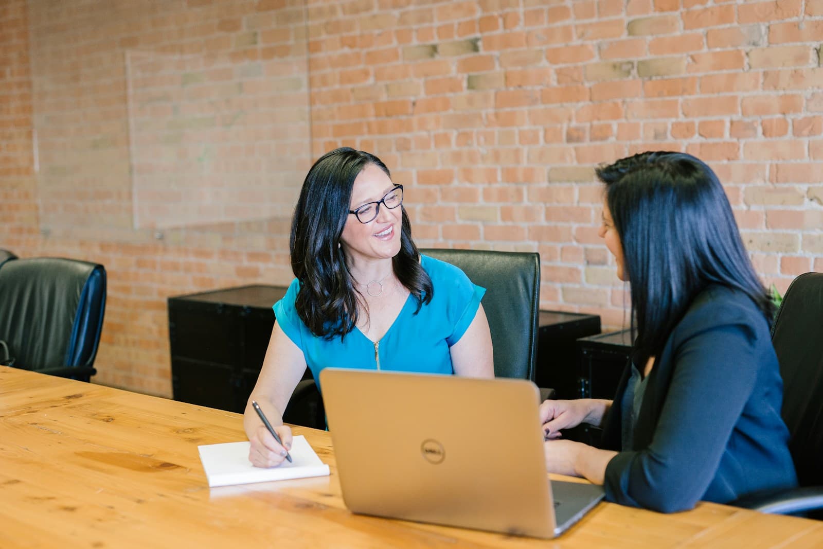 Two women working together at a conference table in a brick-walled office