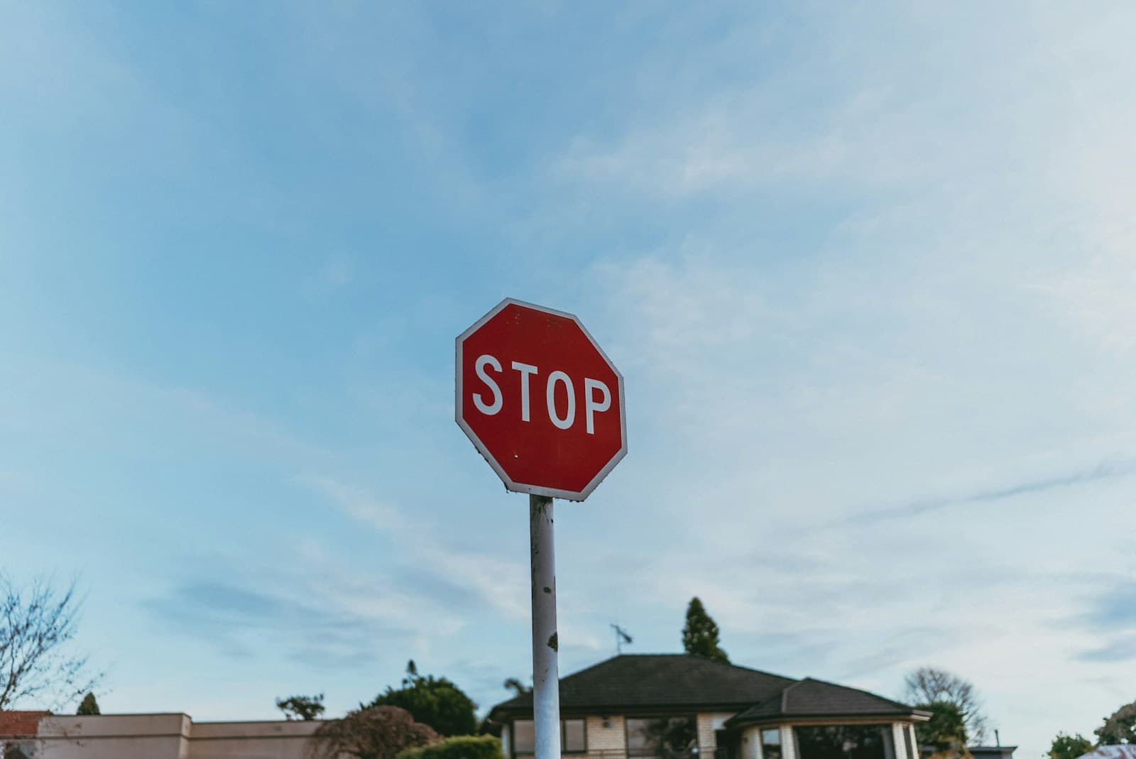 Red stop sign on pole with residential house and blue sky in background