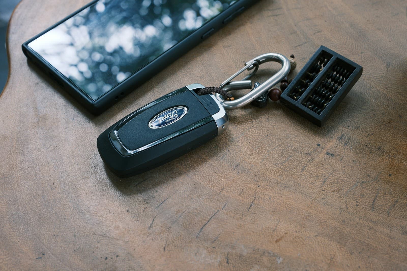 Black Ford key fob on a wooden surface beside a smartphone