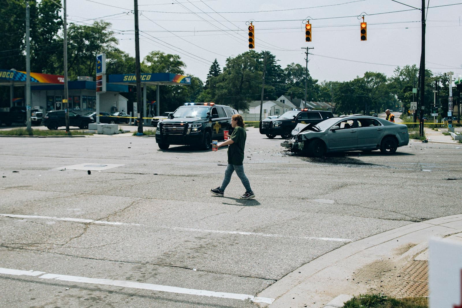 Person walking across street intersection with cars and traffic lights in urban commercial area