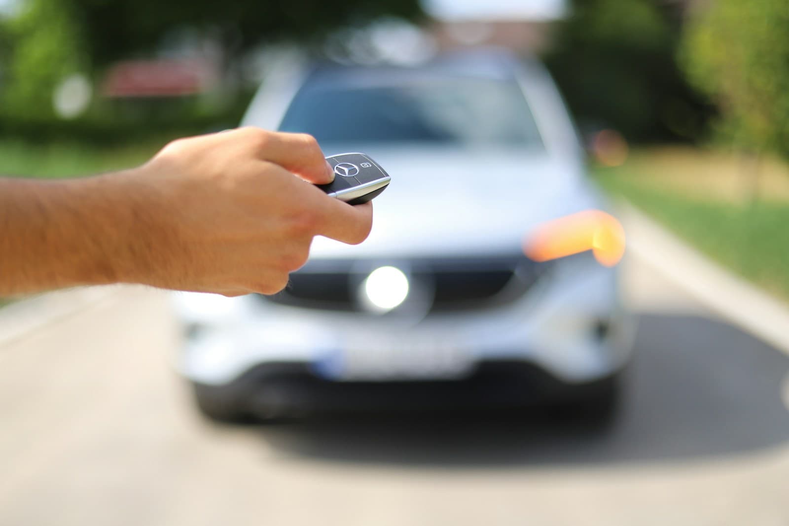 Hand holding car key remote pointing at white car on street