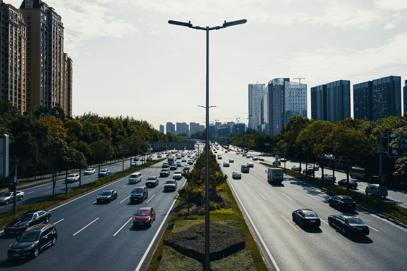 Multi-lane urban highway with traffic flowing between high-rise buildings and trees on both sides